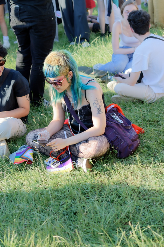 21 - Person sitting on grass, wearing patterned tights and a dark top with a backpack nearby